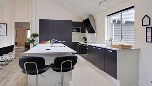 Una cocina moderna con una isla central, taburetes negros y una ventana con persianas.