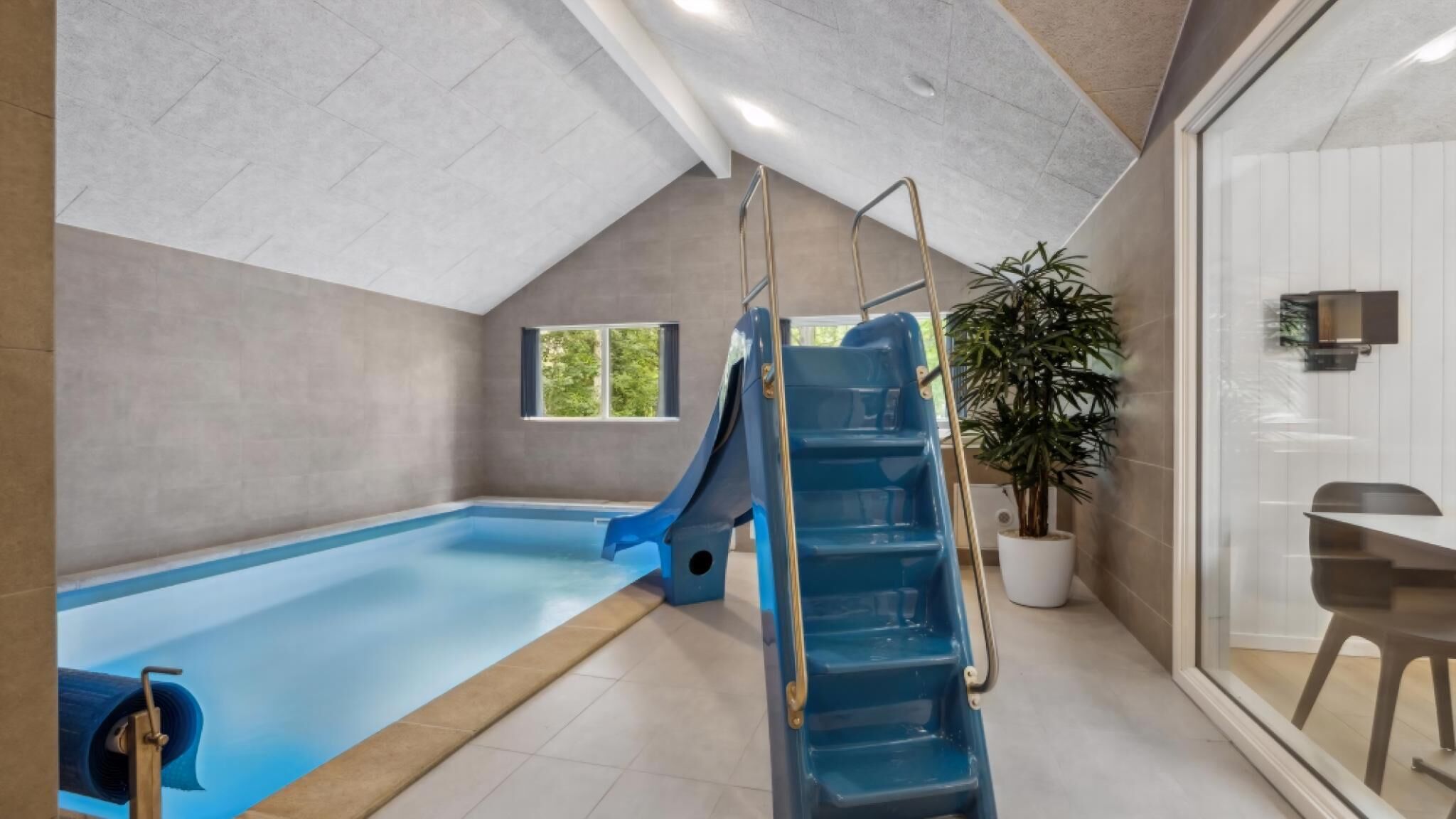 A swimming pool with a slide, a potted plant, and a seating area.