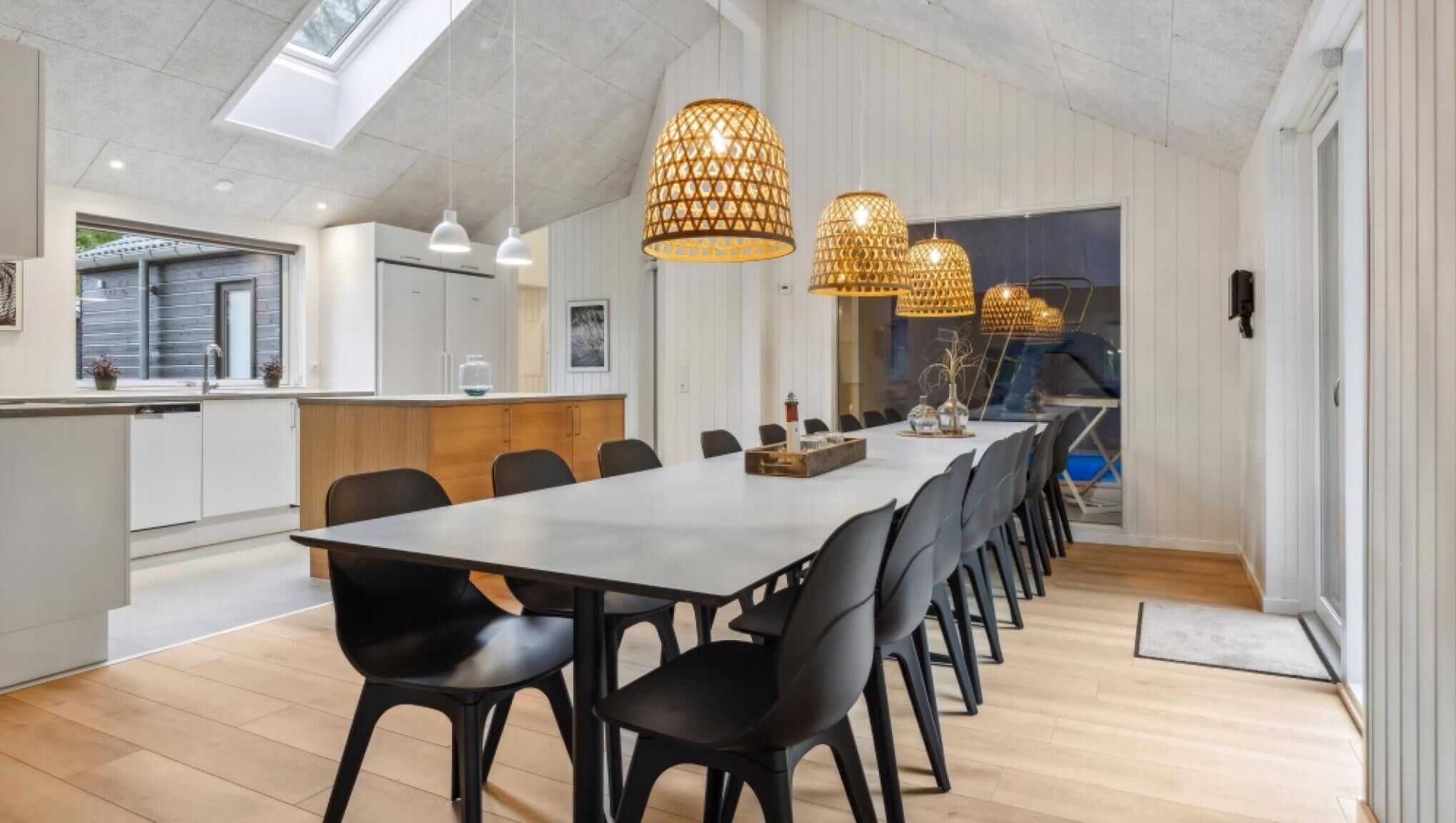 Een moderne keuken met een lange eettafel, zwarte stoelen en hanglampen.
