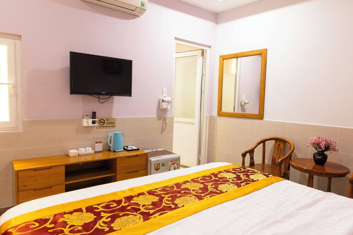 A hotel room with a bed, a television, a desk with a telephone, a coffee maker, and a small table with a vase of flowers.