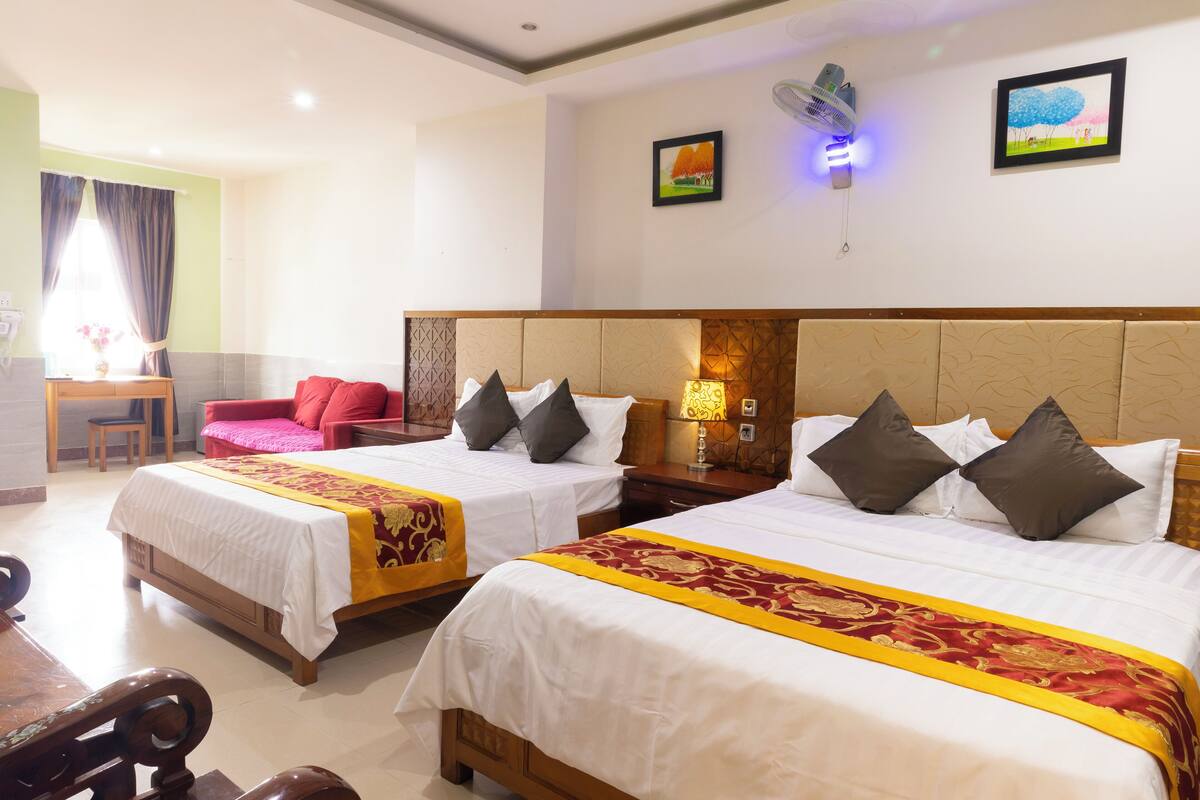 A hotel room with two beds, a desk, a chair, and a red sofa.