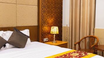 A hotel room with a bed, pillows, a nightstand with a lamp, a wooden chair, and a curtain.