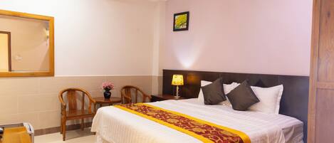A hotel room with a large bed, a wooden nightstand, a chair, a desk, and a mirror on the wall.