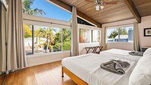 Una habitación de hotel con una cama grande, dos camas más pequeñas, un ventilador de techo y ventanas amplias con cortinas.