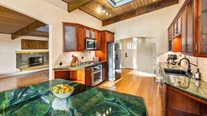 Una cocina amplia con armarios de madera, una isla grande con un cuenco de fruta, un tragaluz y vistas al área de estar.
