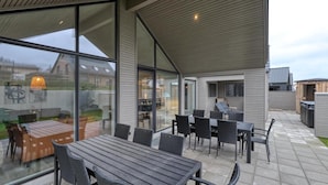 Un patio moderno al aire libre con una mesa y sillas de madera, amplias ventanas de vidrio y vistas al jardín.