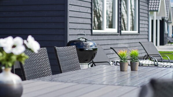 Un patio con una parrilla, sillas y plantas en macetas.