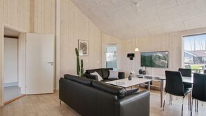 Un salon moderne avec un canapé en cuir noir, une table à manger avec des chaises, un téléviseur à écran plat et une grande fenêtre donnant sur l’extérieur.