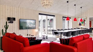 Un salon moderne avec un canapé rouge, un téléviseur à écran plat et un coin repas éclairé par des suspensions rouges.