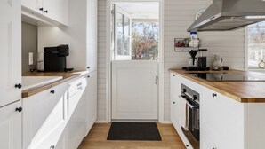 Une cuisine moderne avec des meubles blancs, une machine à café noire et une hotte en acier inoxydable.