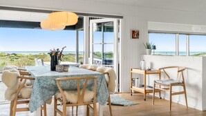 Ein geräumiges Zimmer mit großem Tisch und Stühlen, Blick auf den Strand und einer Tür, die nach draußen führt.