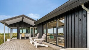 Eine Holzterrasse mit Sitzgelegenheit im Freien, einem Whirlpool und großen Fenstern mit Blick auf die Landschaft.