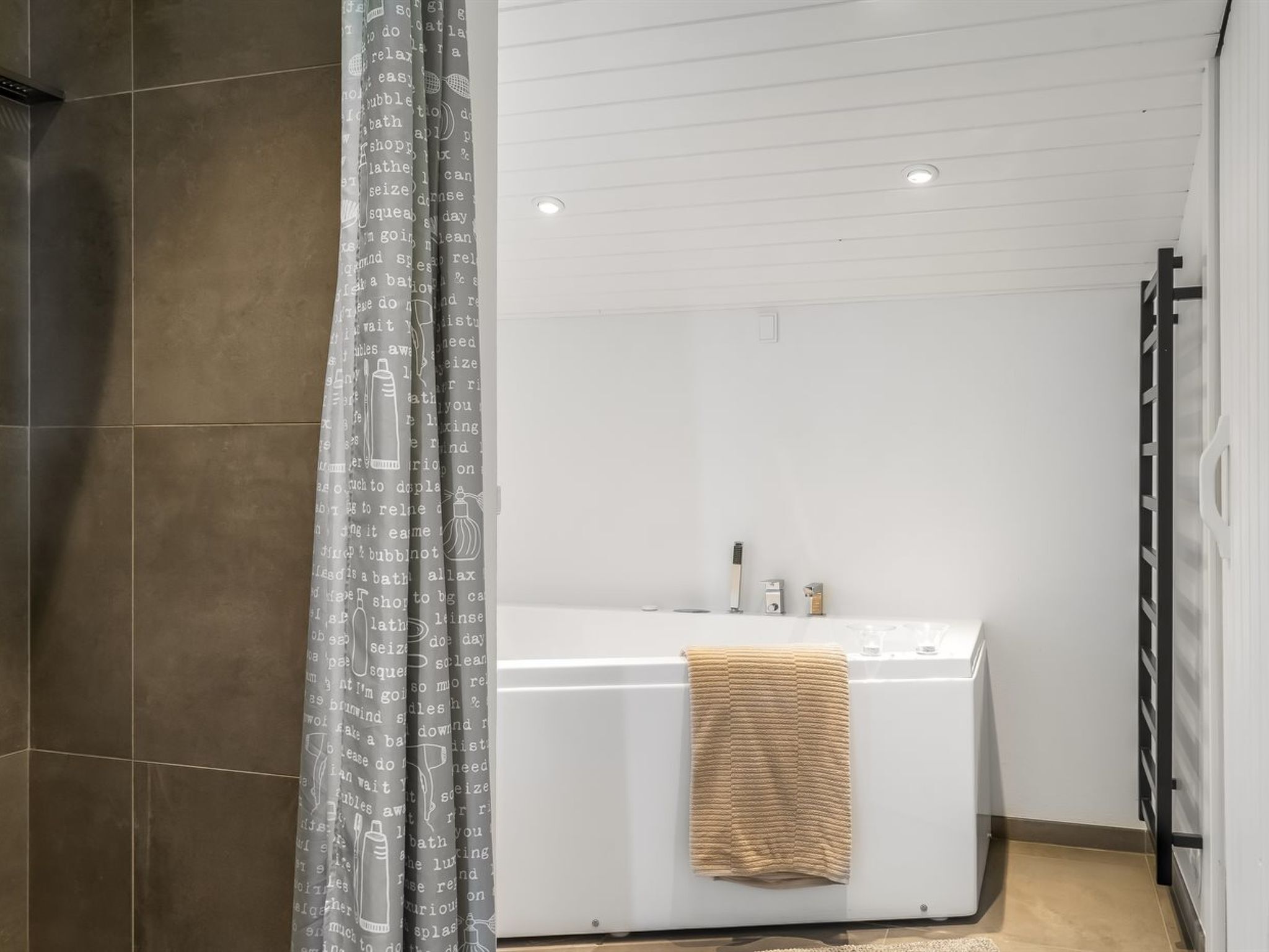 Un baño moderno con una bañera blanca, una toalla y una cortina de ducha con texto.