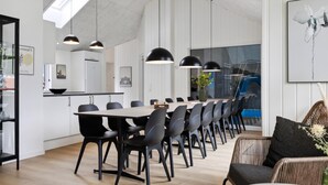 Un comedor moderno con una mesa larga, sillas negras, luces colgantes y una silla de mimbre con cojín.
