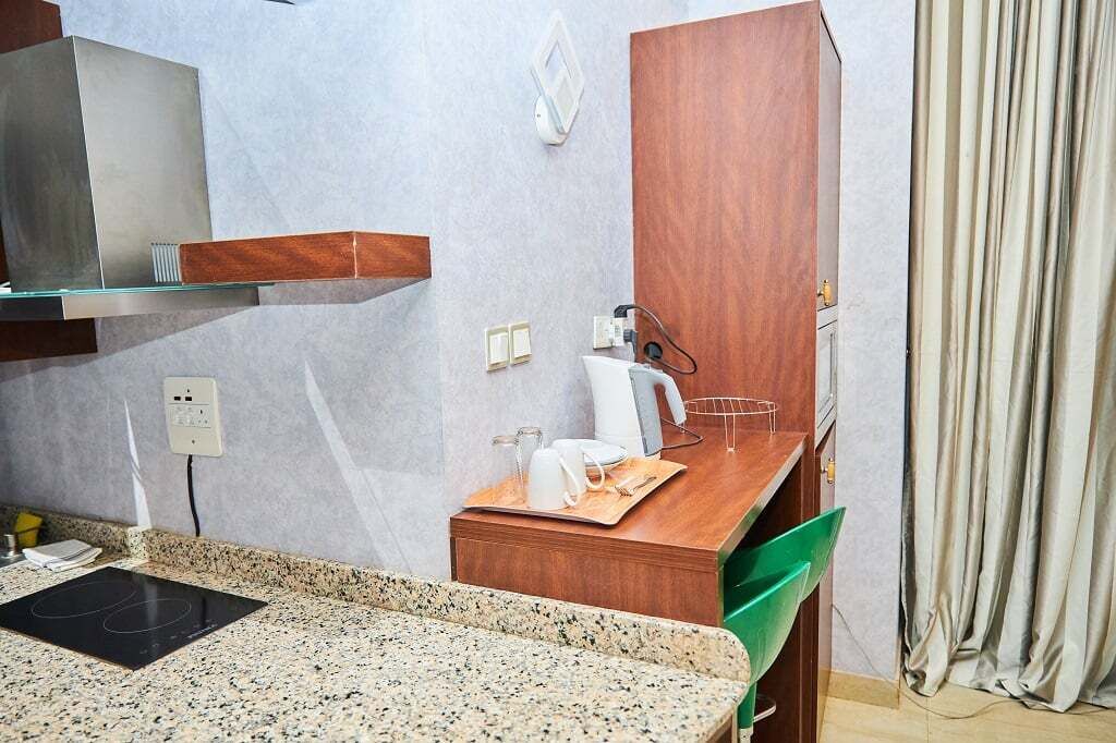 A compact kitchen with a granite countertop, a built-in stove, a wooden cabinet, and a small dining area with a tray of breakfast items.