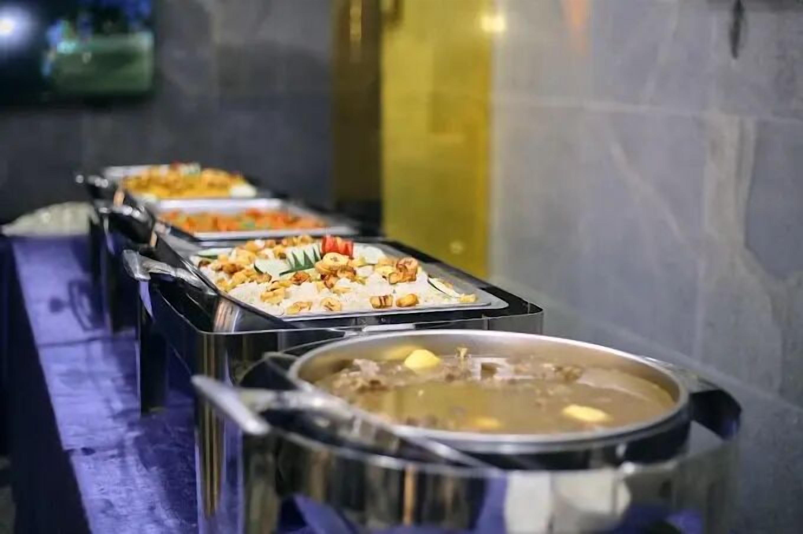 A buffet line with various dishes, including rice, vegetables, and a large pot of soup.