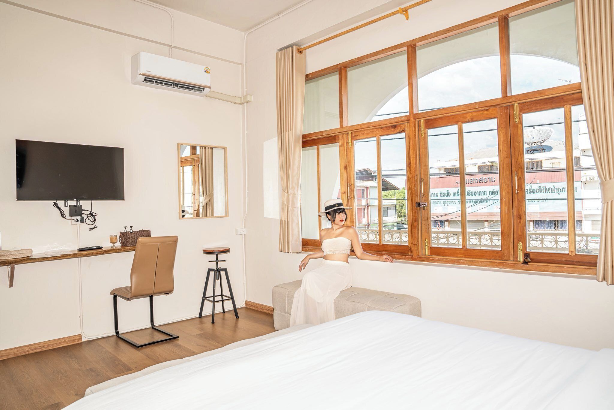 Una habitación de hotel con cama, escritorio con silla, televisión y un ventanal con cortinas.
