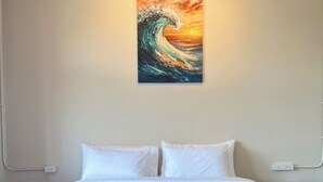 Hotelkamer met een bed, witte beddengoed, een schilderij van een golf en een netjes opgevouwen handdoek op de voetenbank.