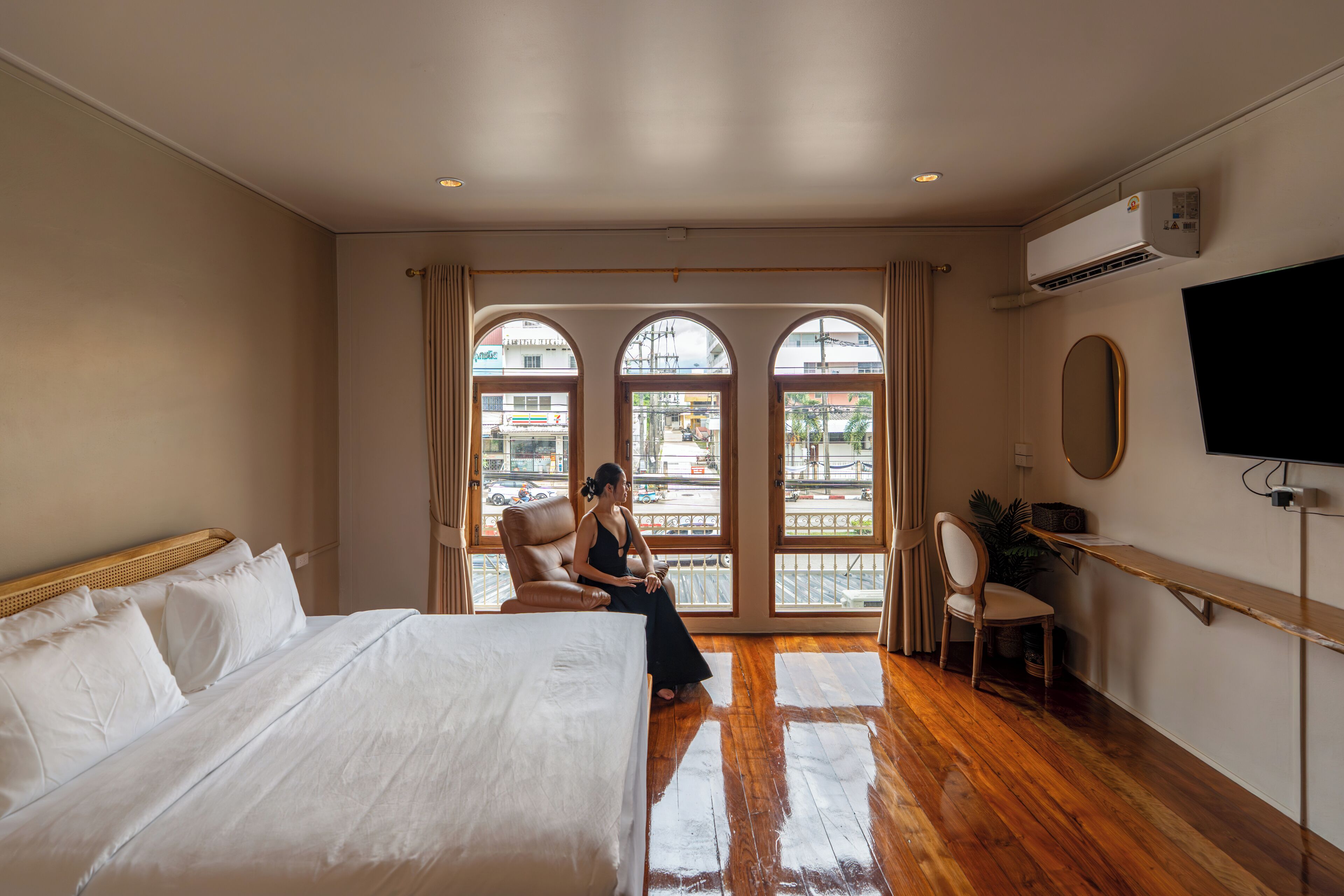 Ein Hotelzimmer mit einem großen Bett, einem Schreibtisch, einem Stuhl und einem Fernseher. Es gibt Fenster mit Vorhängen und eine Klimaanlage an der Wand.