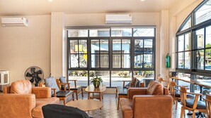Een moderne lounge met leren banken, houten tafels en grote ramen met uitzicht op de straat.