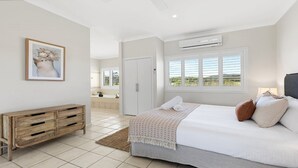 Ein Schlafzimmer mit einem Bett, einer Holzkommode, einem Gemälde, einer Klimaanlage und einem Fenster mit Jalousien.