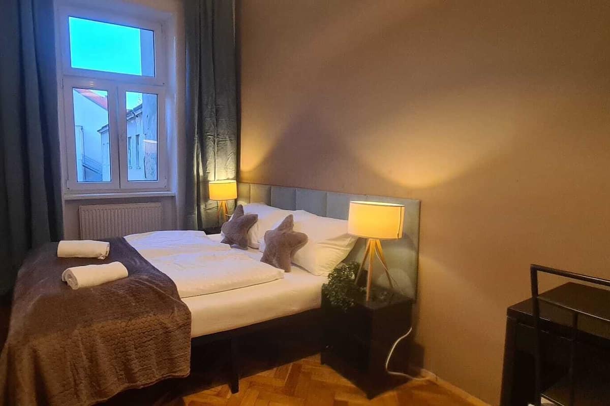 A hotel room with a bed, two bedside lamps, a window, and a nightstand.