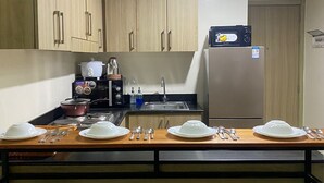 Cocina moderna con armarios de madera, microondas, estufa y lavaplatos. Hay cuatro taburetes y una mesa de comedor preparada para cuatro comensales.