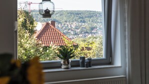 Blick aus dem Fenster auf eine Stadt mit einem Gebäude mit rotem Dach, viel Grün und einem Kran in der Ferne.