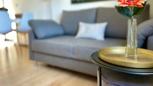 Ein Wohnzimmer mit grauem Sofa, einem Couchtisch mit Blumenvase und einem Bild an der Wand.