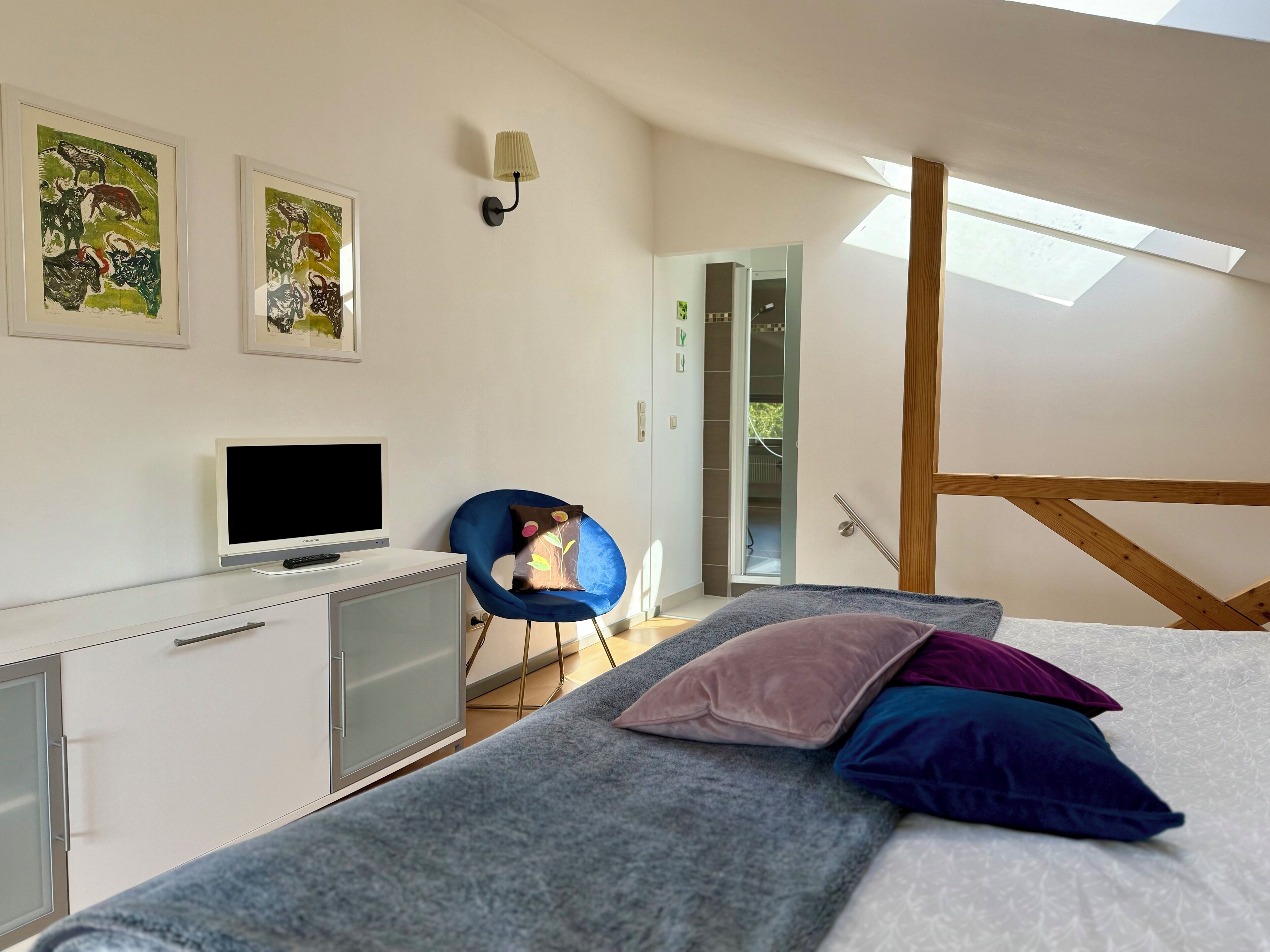 A modern bedroom with a bed, a desk with a computer, a chair, and artwork on the wall.