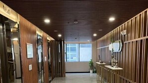 A modern hallway with a polished marble floor, wooden paneling on the walls, and a glass elevator on the left. - Skyport Hotel (Parañaque)