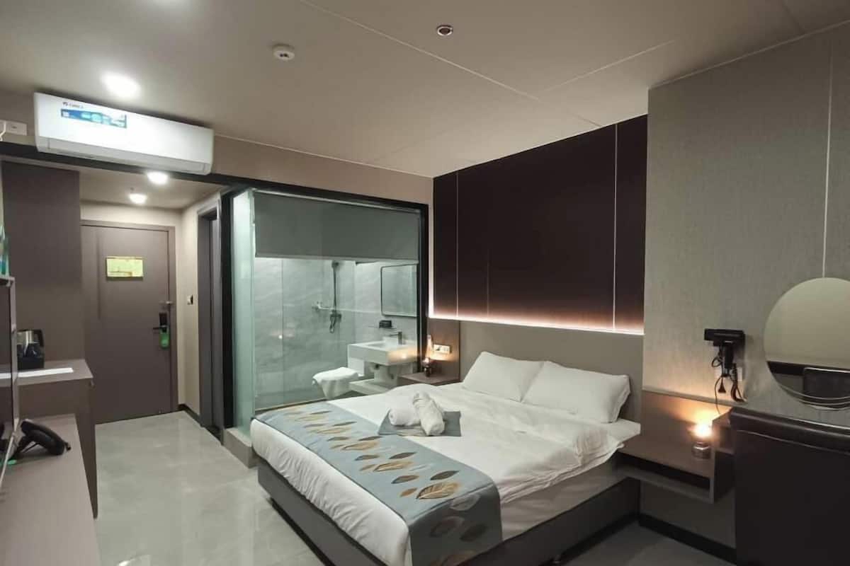 A modern hotel room with a large bed, a glass-enclosed shower, a bedside table, and a built-in mirror.