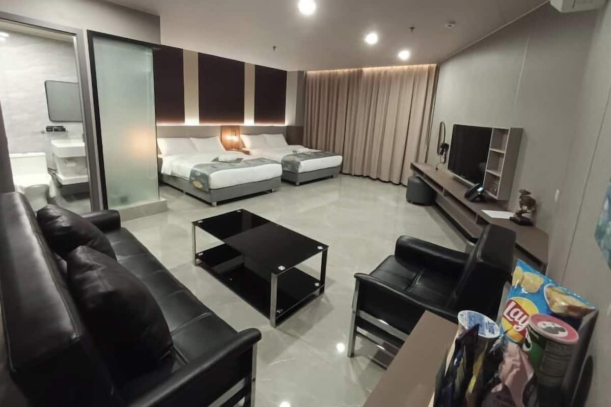 A modern hotel room with a sofa, two beds, a TV, and a coffee machine.