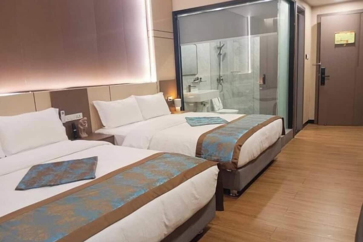 A hotel room with two beds, a glass shower enclosure, and a wooden floor.