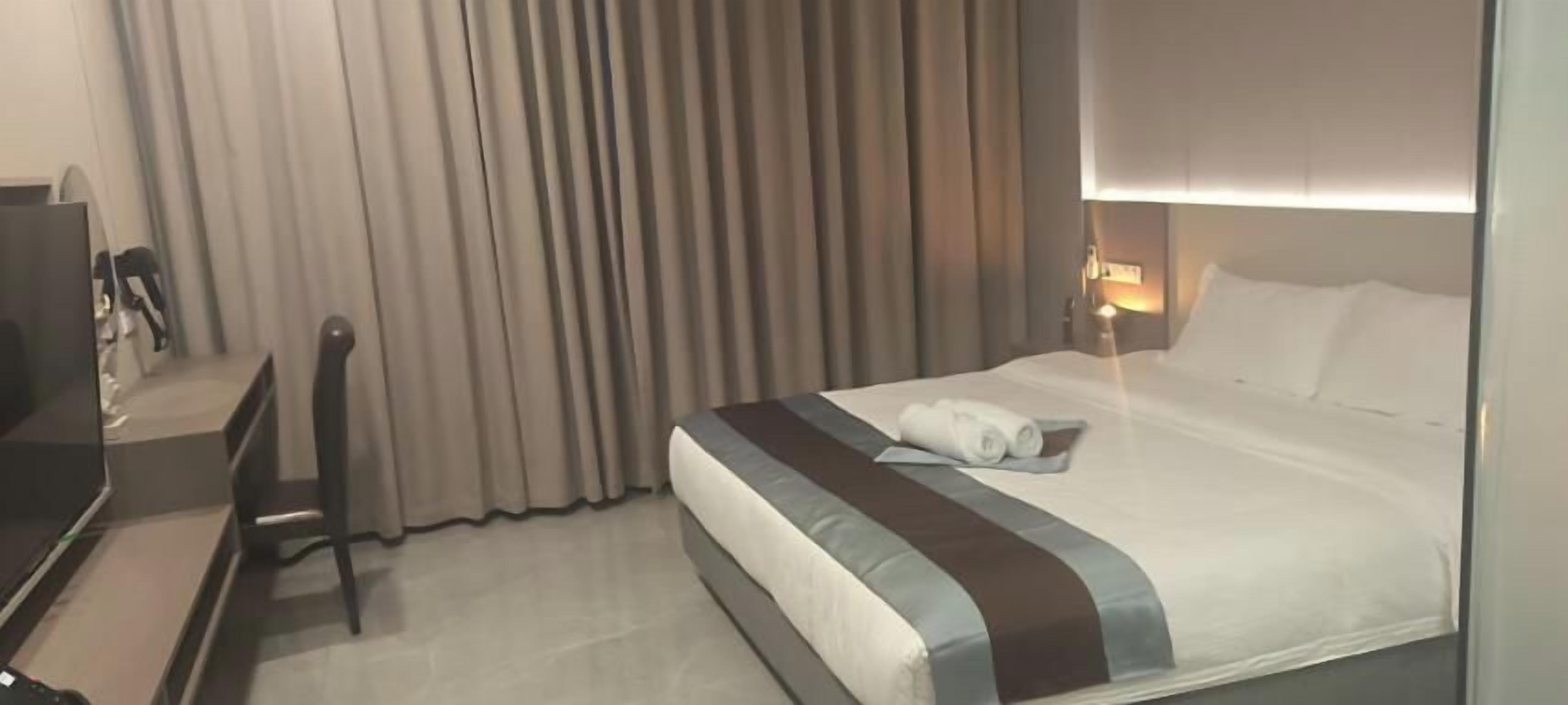 A hotel room with a bed, a desk, a chair, and a curtain.