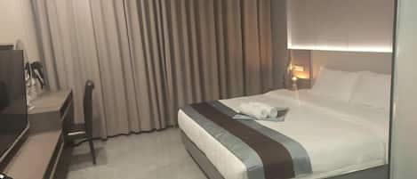A hotel room with a bed, a desk, a chair, and a curtain.