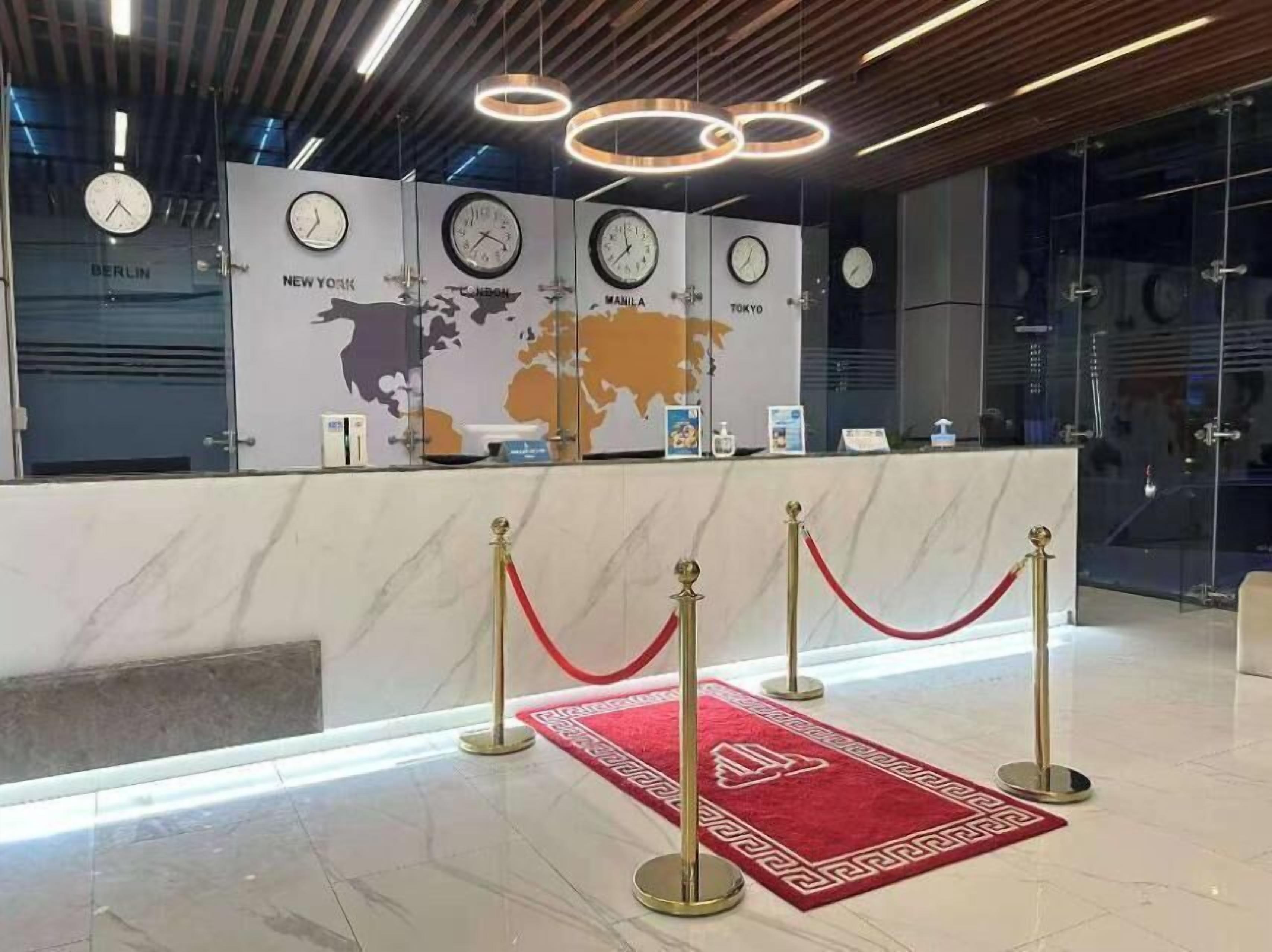 A reception area with a marble counter, clocks displaying times from various cities, and a world map backdrop.