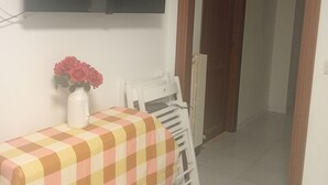 Una habitación con una cama, una mesa con mantel a cuadros, un florero con flores y un televisor montado en la pared.