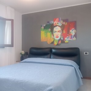 Une chambre à coucher avec un lit, une tête de lit, un tableau accroché au mur et une fenêtre avec des rideaux.