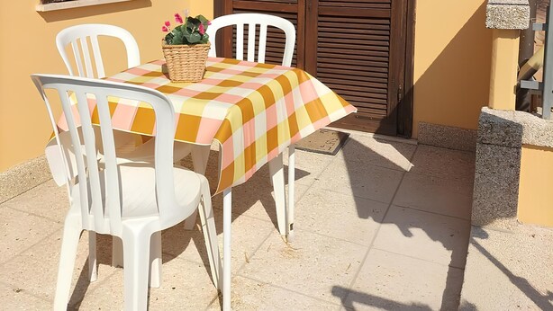 Un patio con una mesa, sillas, el número '10' en la pared y una puerta de madera cerrada.