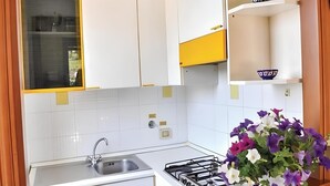 Una cocina compacta con gabinetes blancos y amarillos, un lavamanos de acero inoxidable y una estufa a gas.