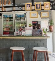 Una zona de bar con un refrigerador lleno de bebidas, una pizarra con el menú y cuadros en la pared.