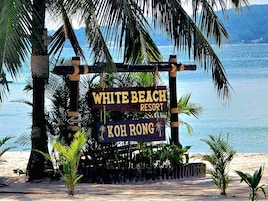 Un letrero de madera con la inscripción 'WHITE BEACH RESORT' y 'KOH RONG', rodeado de palmeras y vistas a la playa.