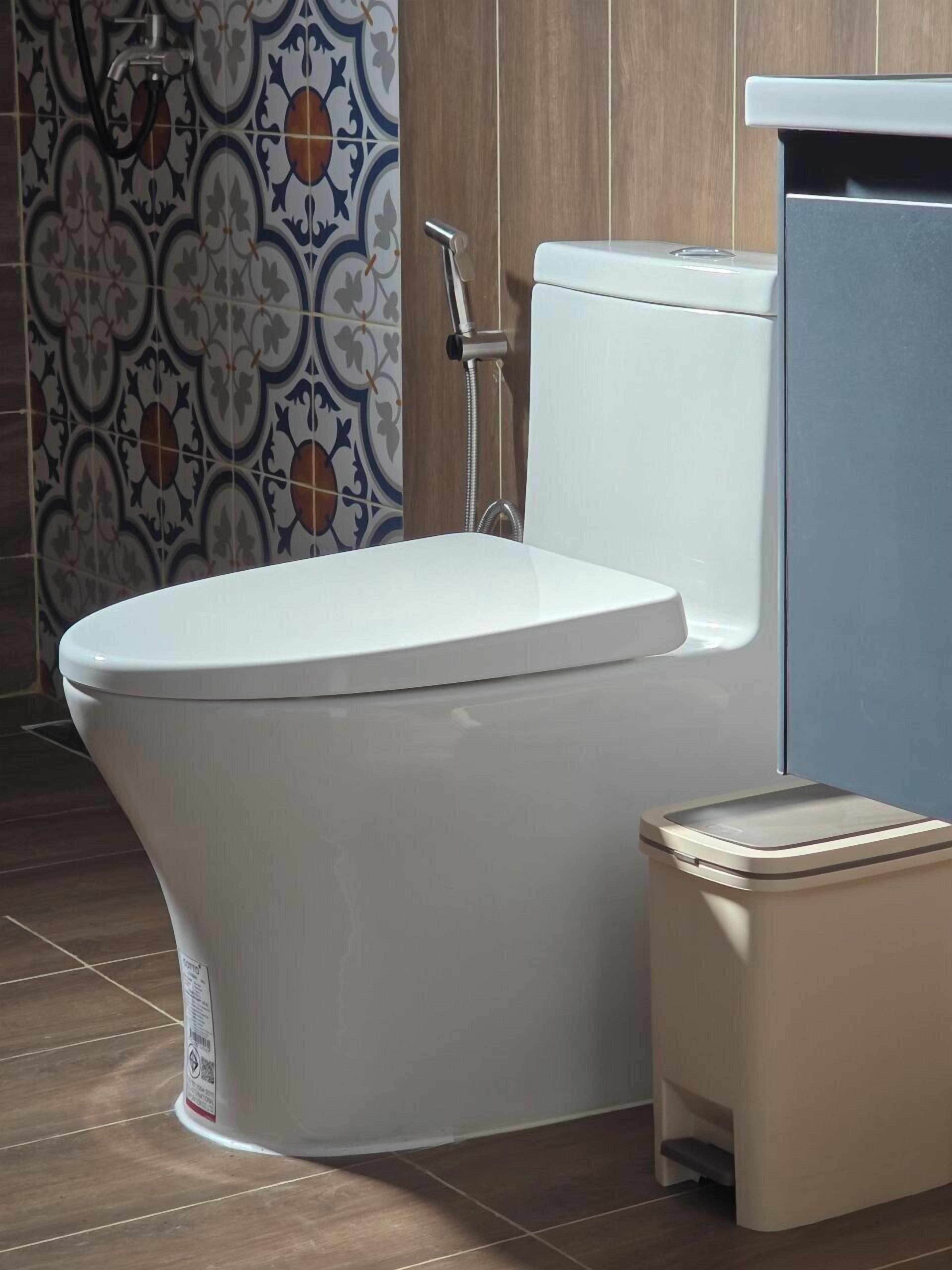 A modern bathroom with a white toilet, a shower, and a small trash bin.
