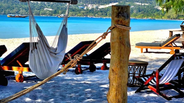A hammock tied to a wooden post on a sandy beach with lounge chairs and a view of the sea. - WHITE BEACH RESORT LONGSET (Koh Rong)