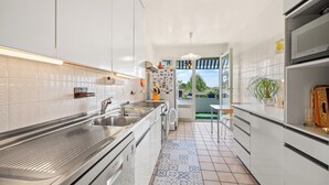 A modern kitchen with white cabinets, stainless steel appliances, a tiled backsplash, and a view through a door to an outdoor area. - Taverney | Spacious, bright apartment (Geneva) (Le Grand-Saconnex)