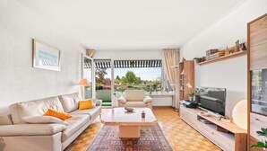 A modern living room with a sofa, armchair, coffee table, TV, and a view of the outdoors. - Taverney | Spacious, bright apartment (Geneva) (Le Grand-Saconnex)