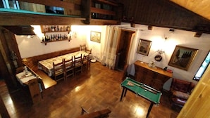 A dining area with a wooden table and chairs, a billiards table, and a shelf with bottles.