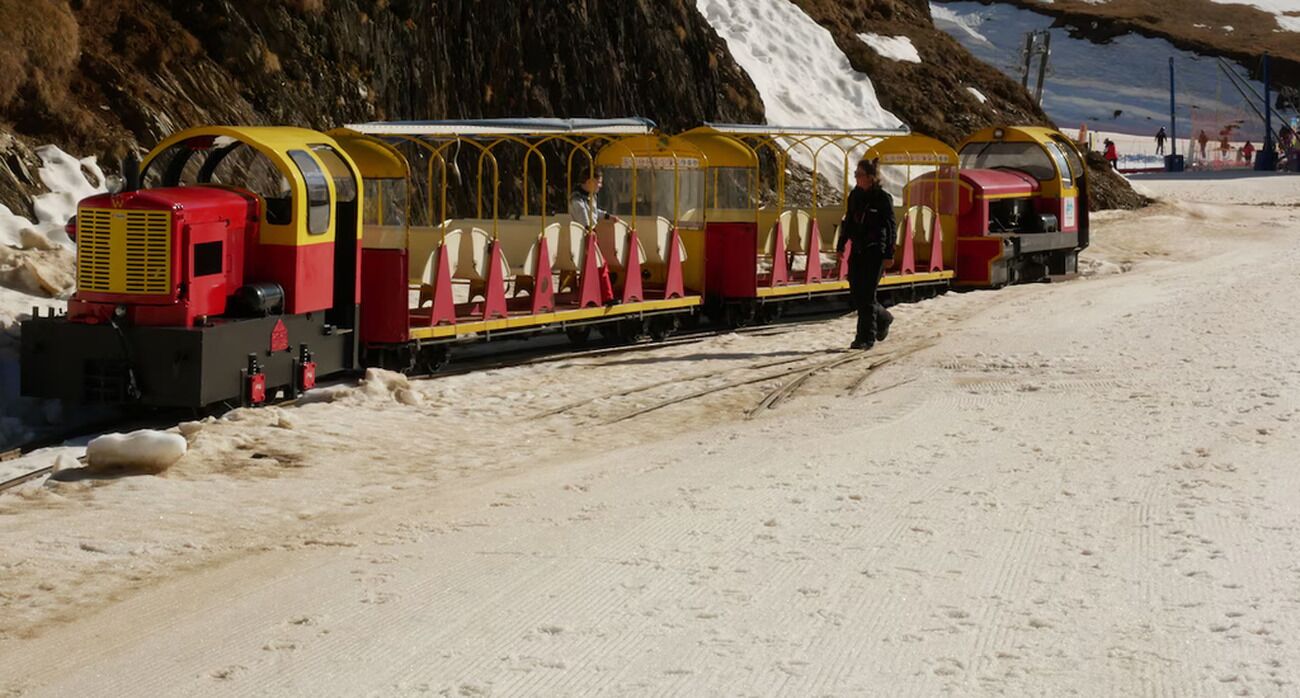 A small, enclosed train with yellow and red colors, running on tracks in a snowy area.