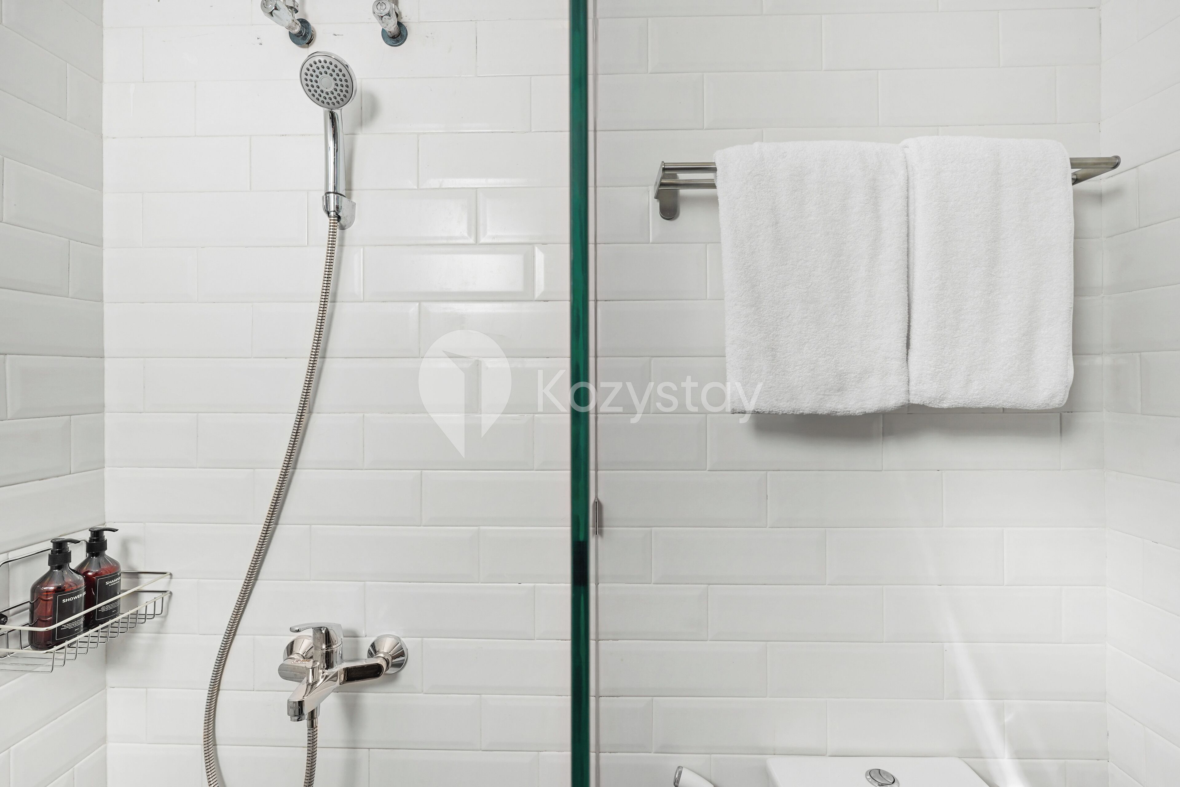 A modern bathroom with a glass shower enclosure, a towel rack with two white towels, and a soap dispenser on a shelf.